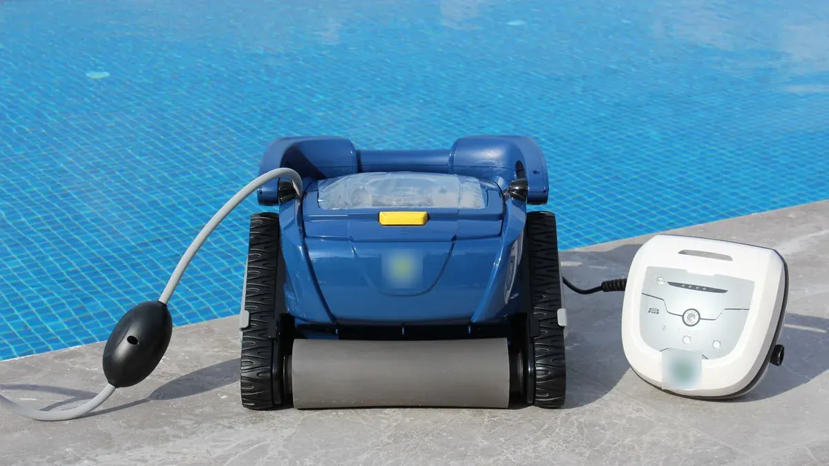 Robot limpiafondos eléctrico con orugas, su cable y su caja de alimentación, apoyados en el borde de una piscina.